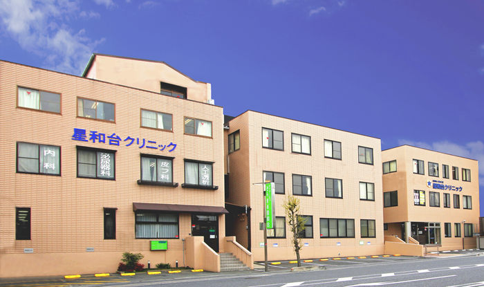 介護施設の建物外観。ベージュ色の複数棟からなる施設。青空が映える。